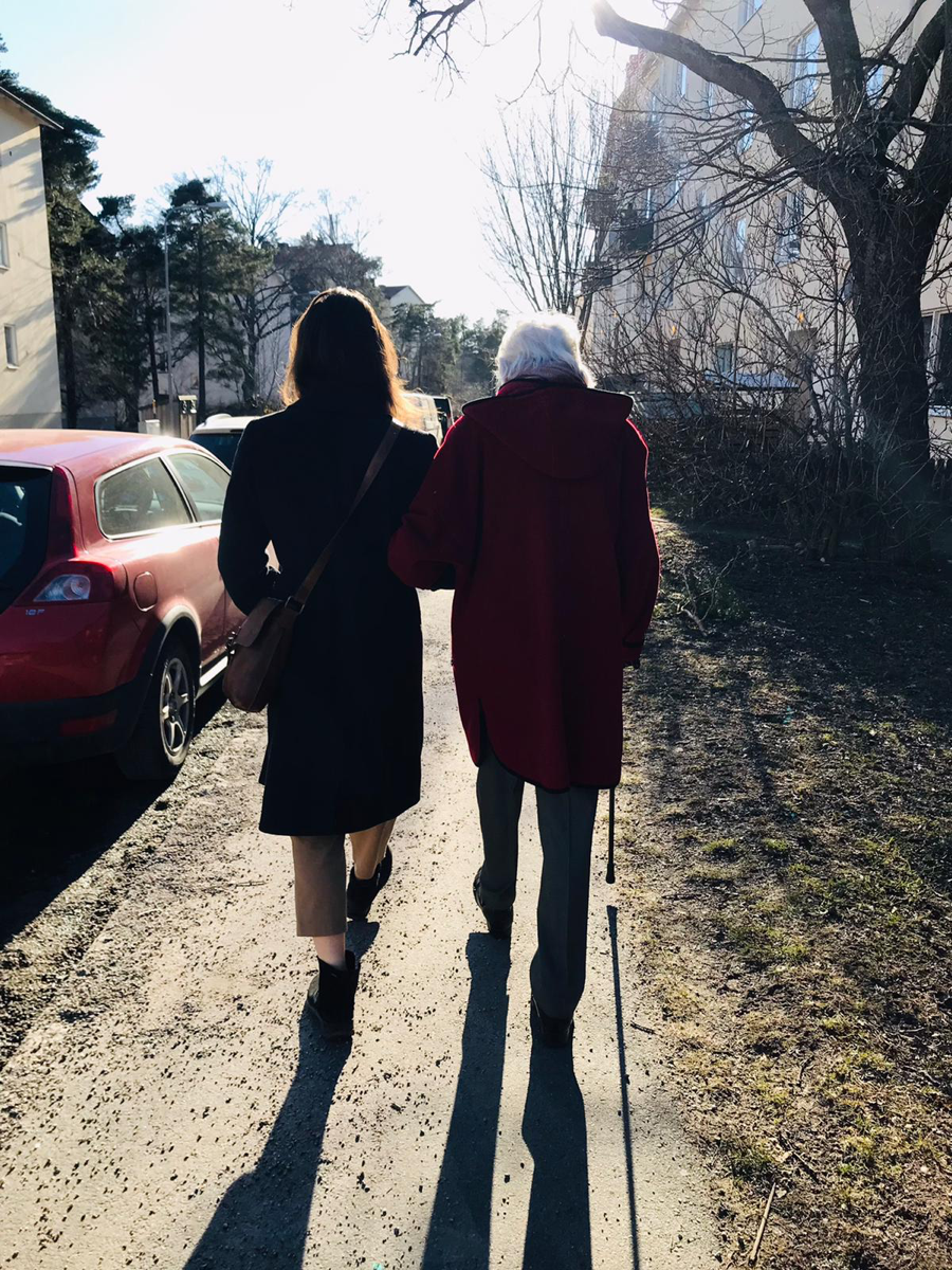 Två personer promenerar arm i arm längs en solbelyst gångväg